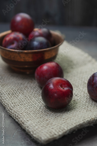 Plums with a bowl on a rural wooden table. Moody and dark style concept. (Prunus domestica)
