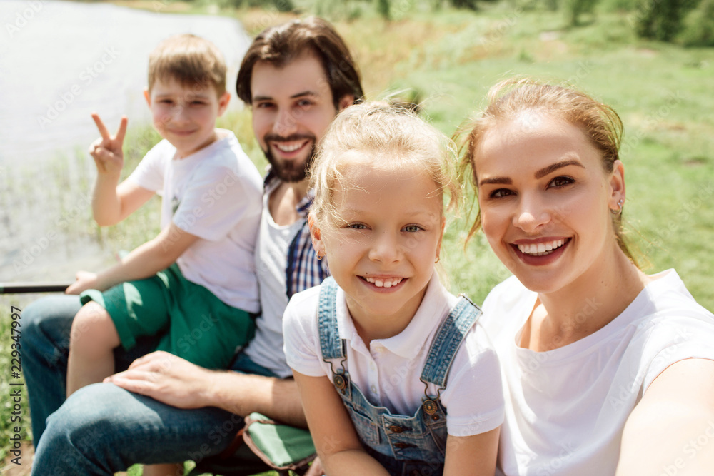 A picture of one family sitting together at the edge of riveer shore. They are looking straight and smiling. Boy is showing piece symbol. A picture of one family sitting together at the edge of riveer shore. They are looking straight and smiling. Boy is showing piece symbol.