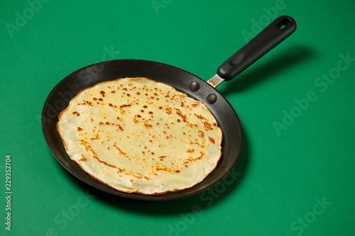 Crepe closeup, thin pancake on a frying pan, green background