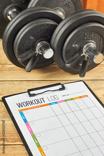 Healthy lifestyle concept. Mock up on workout and fitness dieting diary. Workout log sheet and dumbbells on a wooden background.