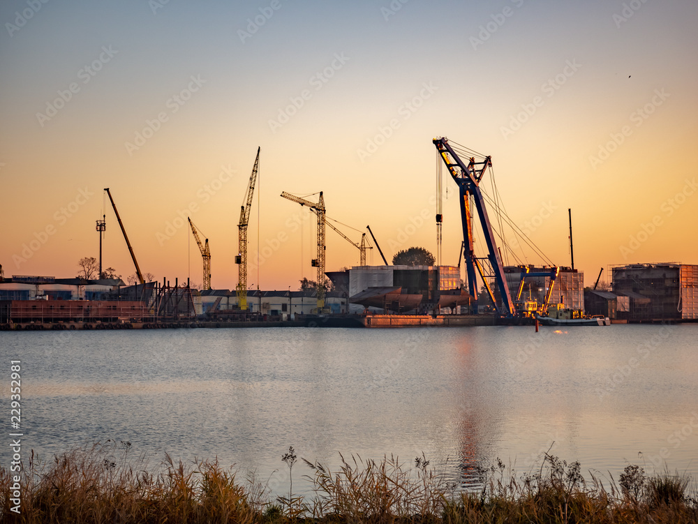 Industrial landscape with shipyard and cranes on river.
