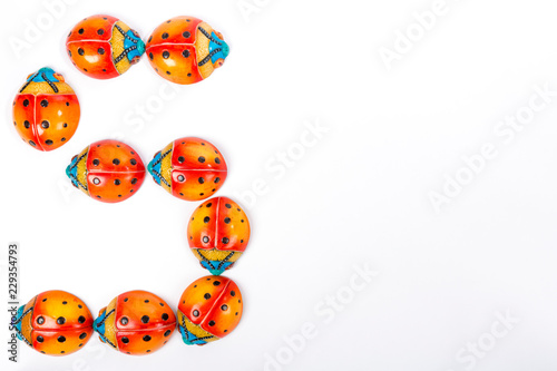 Flat lay with the letter S or the number 5, formed by a group of ceramic ladybugs with red, orange, yellow, blue and black colors on a white background with space for text