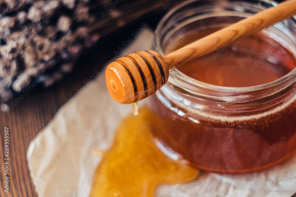 Honey in a jar with a honey dipper on a wooden background with lavender flowers Honey in a jar with a honey dipper on a wooden background with lavender flowers