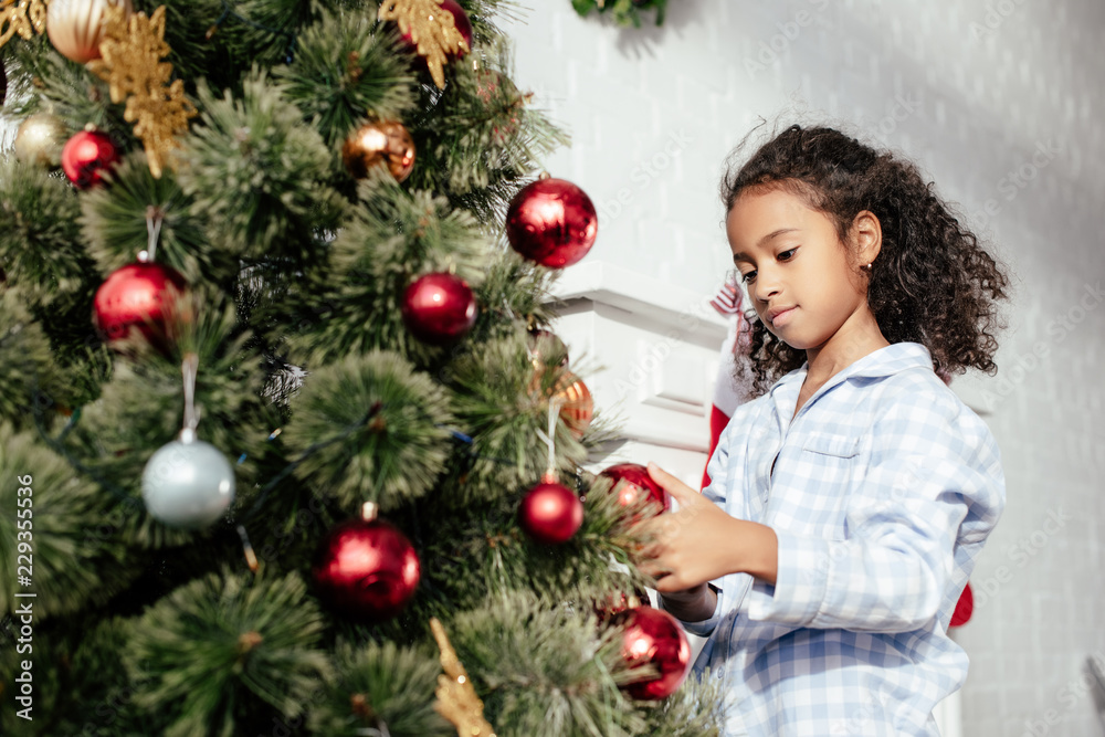 adorable african american child in pajamas decorating christmas tree with red balls at home adorable african american child in pajamas decorating christmas tree with red balls at home