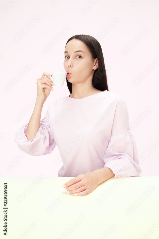 Beautiful lonely woman sitting at pink studio and looking sad holding the cup of coffee in hand. Closeup toned portrait in minimalism style Beautiful lonely woman sitting at pink studio and looking sad holding the cup of coffee in hand. Closeup toned portrait in minimalism style