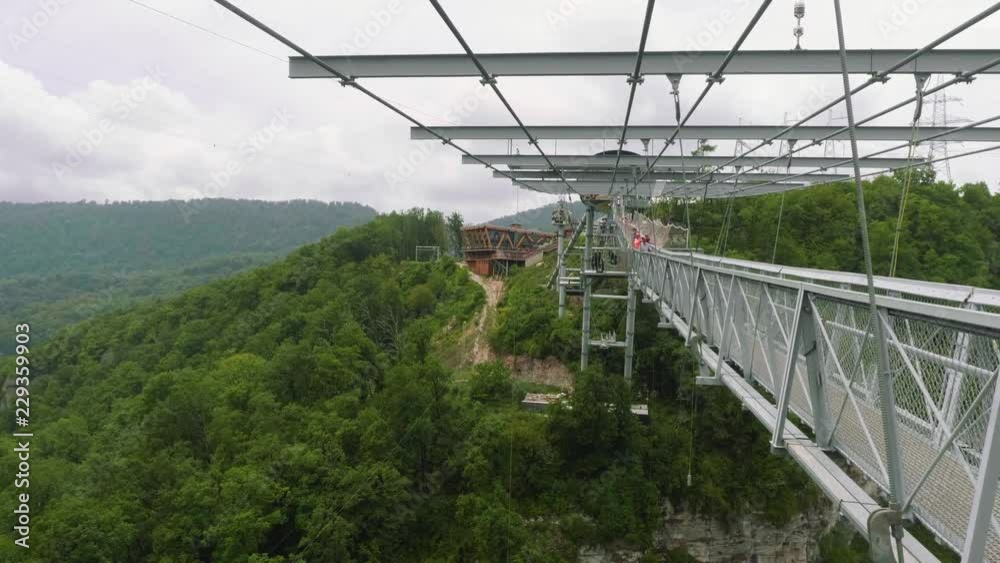 White tourists go on long suspension swinging metal bridge high in mountains White tourists go on long suspension swinging metal bridge high in mountains