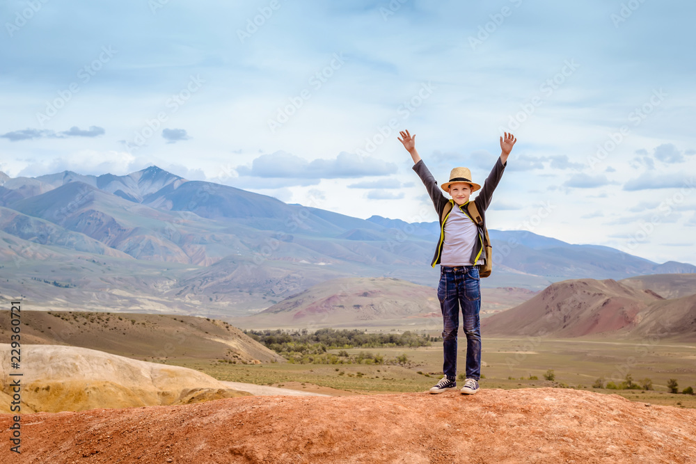 Happy boy traveler with his hands up on blue mountains background Happy boy traveler with his hands up on blue mountains background