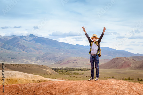 Happy boy traveler with his hands up on blue mountains background