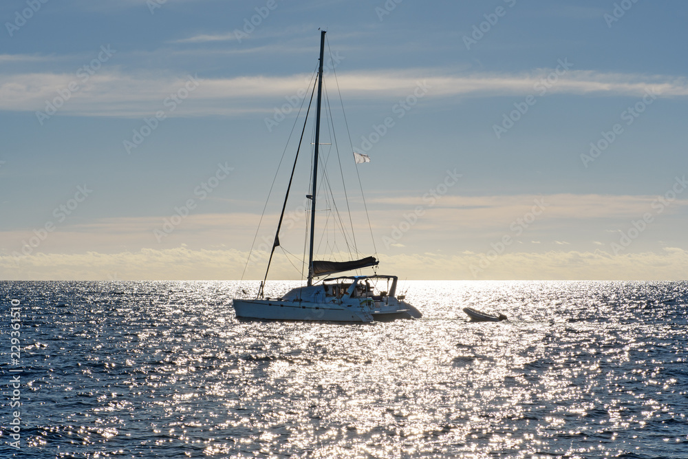 Sailing yacht catamaran in tropical waters at sunset.