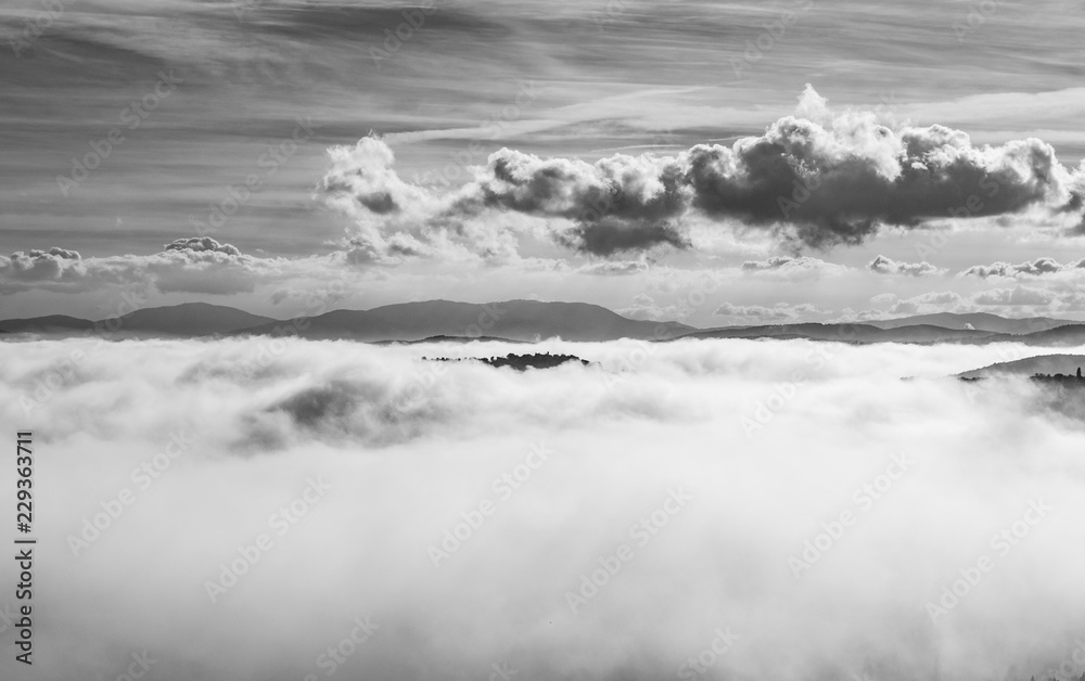 A view from an high tower in the little town of San Gimignano, tuscany italy. A sea made of fog until the horizon with light blue mountains in the background and a little town emerging from the mist 