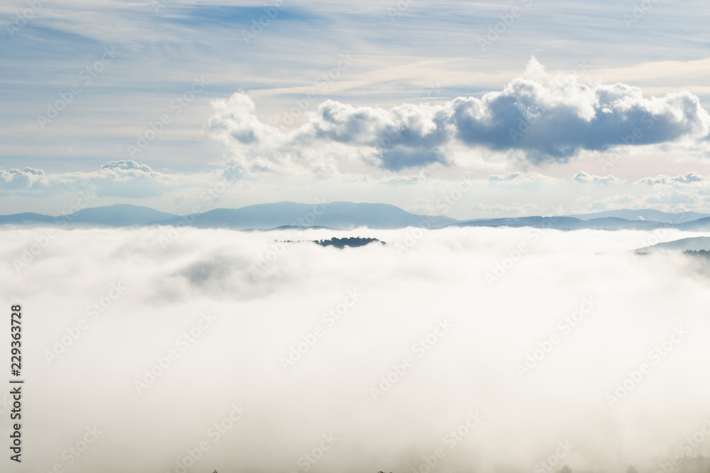 A view from an high tower in the little town of San Gimignano, tuscany italy. A sea made of fog until the horizon with light blue mountains in the background and a little town emerging from the mist A view from an high tower in the little town of San Gimignano, tuscany italy. A sea made of fog until the horizon with light blue mountains in the background and a little town emerging from the mist