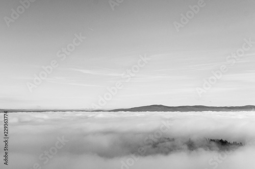 A view from an high tower in the little town of San Gimignano, tuscany italy. A sea made of fog until the horizon with light blue mountains in the background and a little town emerging from the mist 