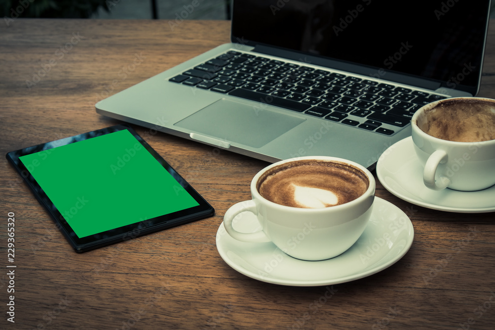 Empty cups and full coffee cup placing together with laptop and green screen tablet on the desk Empty cups and full coffee cup placing together with laptop and green screen tablet on the desk
