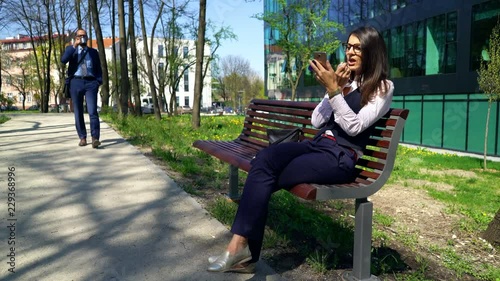 Businesswoman sitting on the bench while businessman is walks next to her, steadycam shot 
