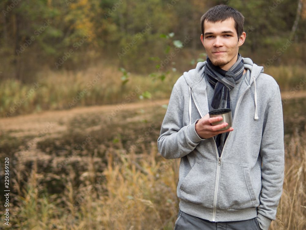 man drinking hot tea from a thermos during a walk through the autumn forest