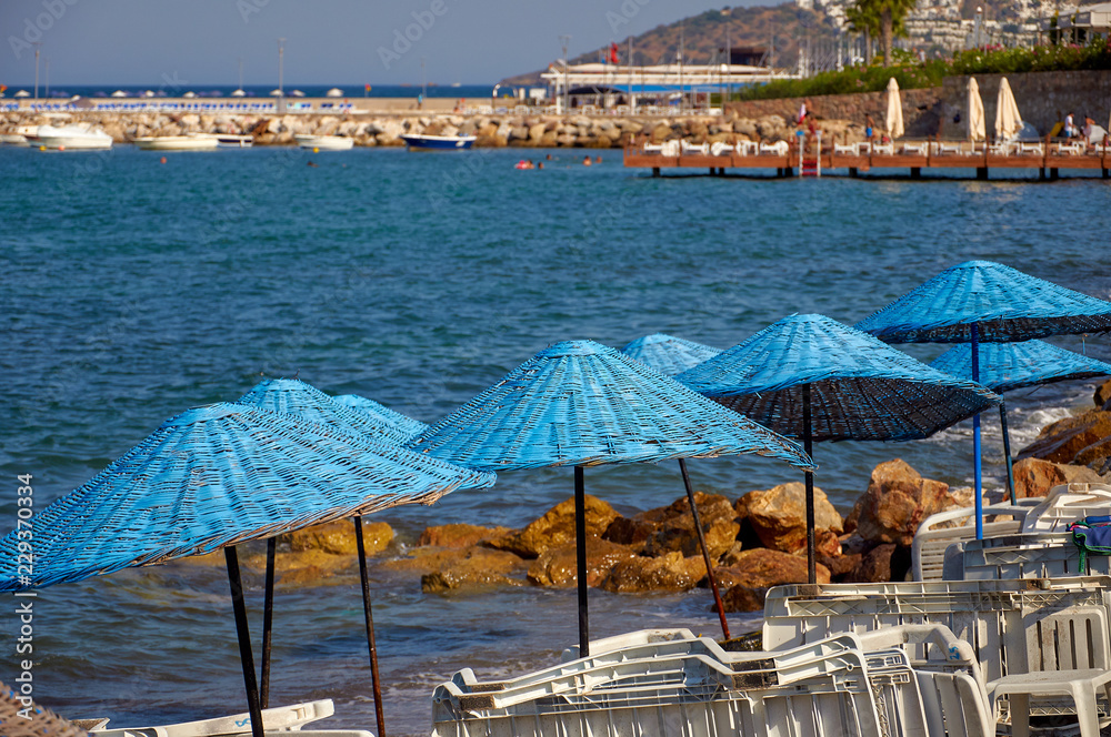 Beach with blue sun umbrellas and loungers. The coast resorts of the Aegean Sea of Turkey. Turgutreis , Bodrum.