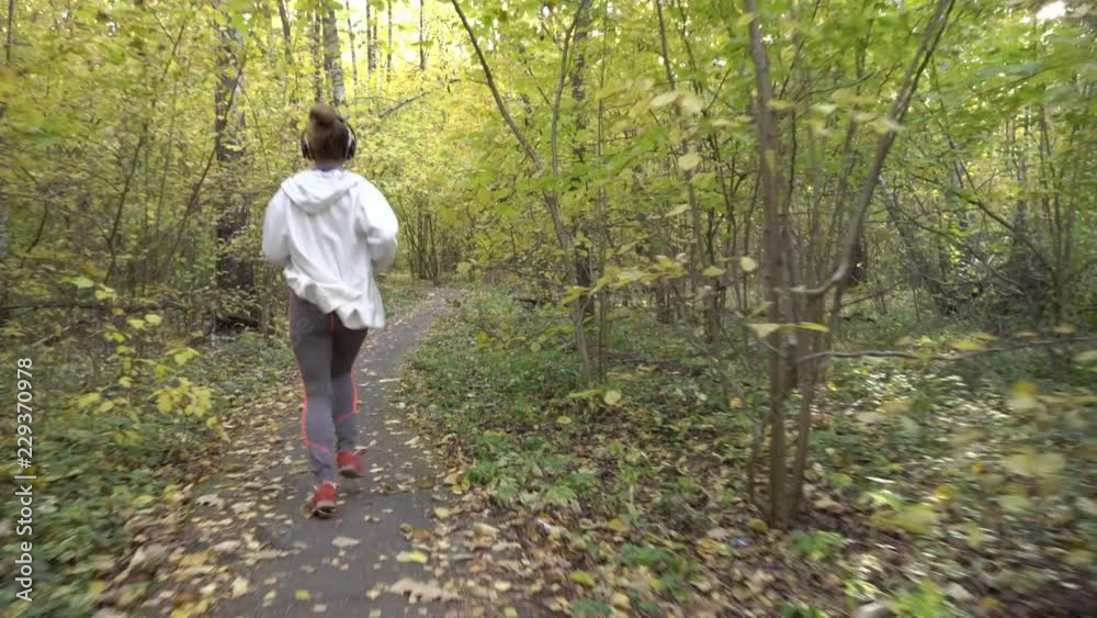 The girl runs in headphones in the autumn forest.
The girl runs in headphones in the autumn forest.