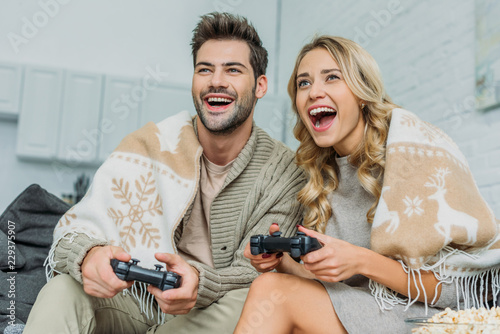 beautiful young couple playing video games and having fun together on couch at home