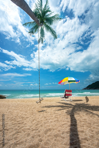 day view of sun sand sea beach with single wood swing and deck chair beach under shadow of coconut tree  relax  comfort and feel free traveling in holidays and vacation