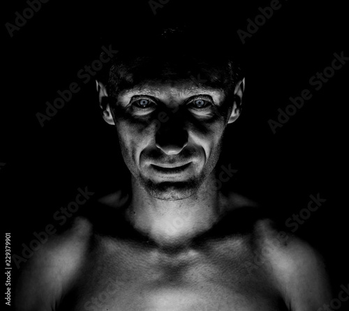 Stylish dark portrait of caucasian man who looks straight at you and looks like maniac. Expressive eyes. Black and white shot, low key lighting.
