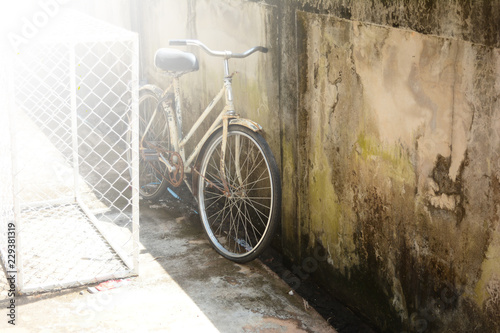 Fototapeta Naklejka Na Ścianę i Meble -  old bicycle parked near the cement wall with bright light from the sun at noon