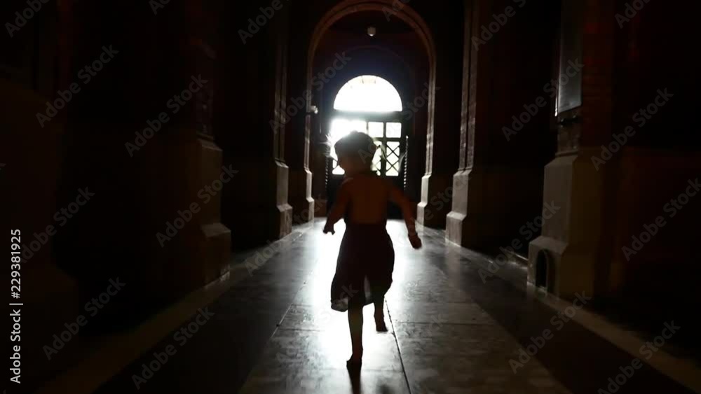 A little girl in a dress is running along the dark corridor among the columns. Playing catch-up. A little girl in a dress is running along the dark corridor among the columns. Playing catch-up.