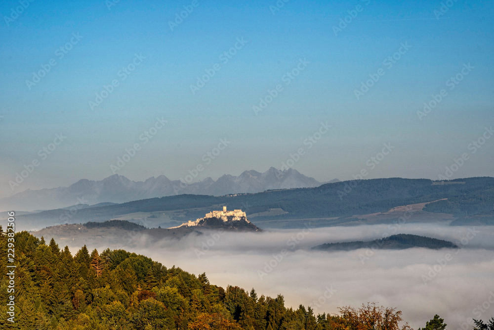 Obraz premium Scenic view of Spis Castle in front of majestic High Tatras mountain range surrounded with morning fog/mist in autumn time.