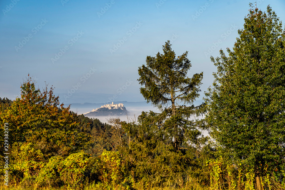 Obraz premium Scenic view of Spis Castle in front of majestic High Tatras mountain range surrounded with morning fog/mist in autumn time.