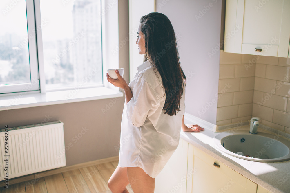 Beautiful and stunning girl stands in kitchen and look to the window. She is strong and well-built. Girl is posing. Beautiful and stunning girl stands in kitchen and look to the window. She is strong and well-built. Girl is posing.
