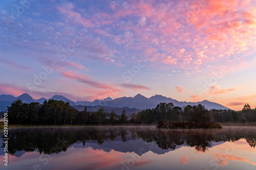 Early morning shot of peaceful scene of beautiful autumn mountain landscape with lake  colorful trees and high peaks and red sky in High Tatras  Slovakia.