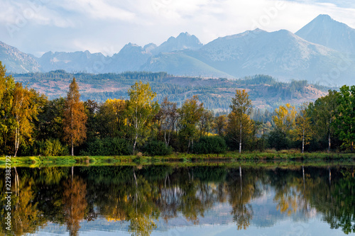 Peaceful scene of beautiful autumn mountain landscape with lake, colorful trees and high peaks in High Tatras, Slovakia.