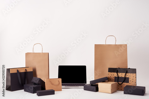 laptop with blank screen with shopping bags and boxes on white surface, black friday concept © LIGHTFIELD STUDIOS