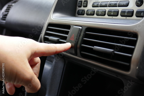 A young Asian woman finger is pushing the emergency sign button at a car console to request a help.