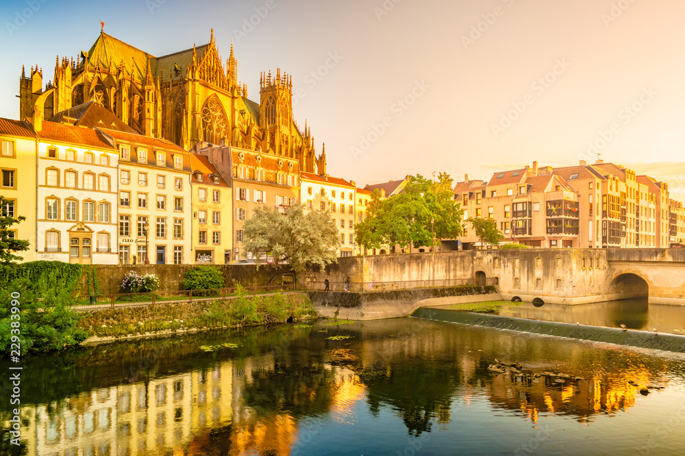 Majestic gothic cathedral of Metz on Moselle river flowing through Metz, with reflections in the water and beautiful sunset sky. France.