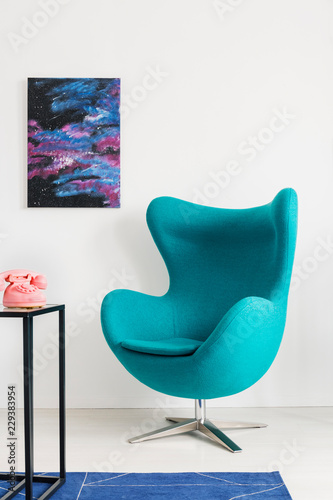 Vertical view of blue egg chair next to metal shelf with pink telephone, cosmos graphic on the wall, real photo with copy space photo