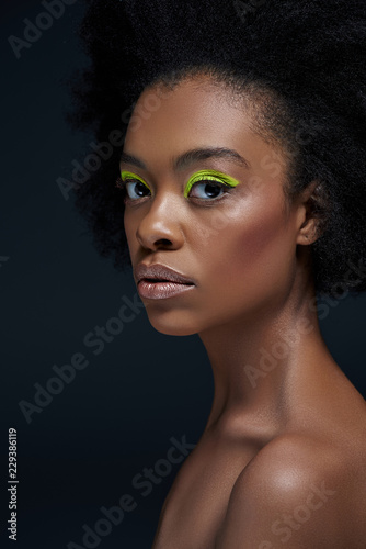 portrait of beautiful african american model with bright neon makeup and bare shoulders isolated on black