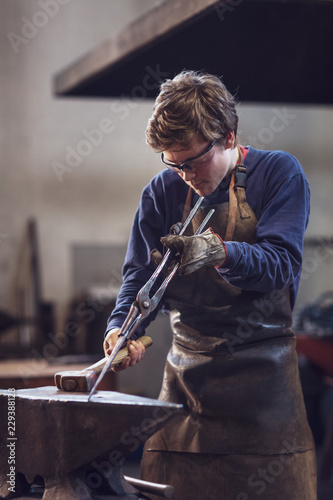 Young blaksmith working with hot metal in a workshop