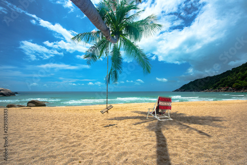 day view of sun sand sea beach with single wood swing and deck chair beach under shadow of coconut tree, relax, comfort and feel free traveling in holidays and vacation
