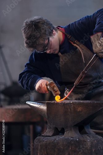 Young blacksmith working with red hot metal