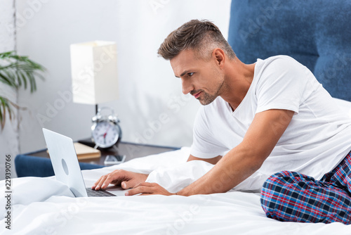 adult male freelancer laying in bed and using laptop during morning time at home