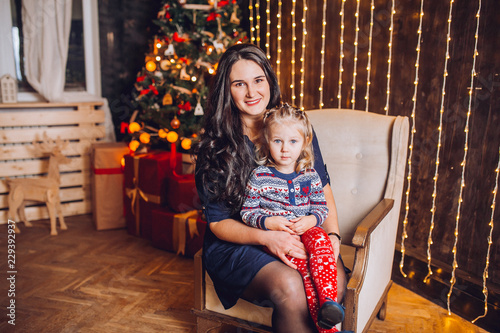 Portrait of beautiful mother and dauther near the Christmas tree. Family woman with little child in a festive New Year's atmosphere. Happy holiday moment. © nataliakabliuk