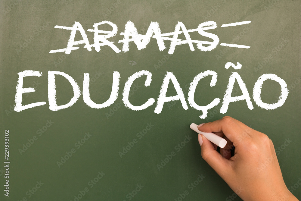 Female hand writing with chalk on green chalkboard Arms and Education (in portuguese). Female hand writing with chalk on green chalkboard Arms and Education (in portuguese).