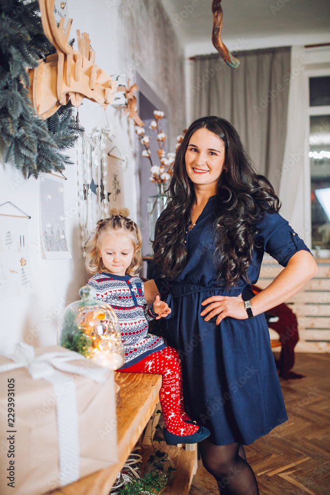 Obraz premium Portrait of beautiful mother and dauther near the Christmas tree. Family woman with little child in a festive New Year's atmosphere. Happy holiday moment.