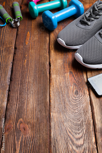 Smartphone, sport shoes and dumbbells on wooden background