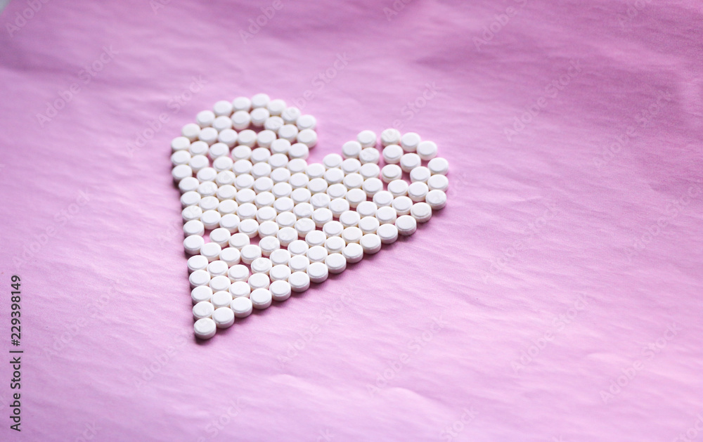 white pills laid out in the shape of a heart on a pink background. concept - heart disease, heart disorders and drugs, cardiology. white pills laid out in the shape of a heart on a pink background. concept - heart disease, heart disorders and drugs, cardiology.