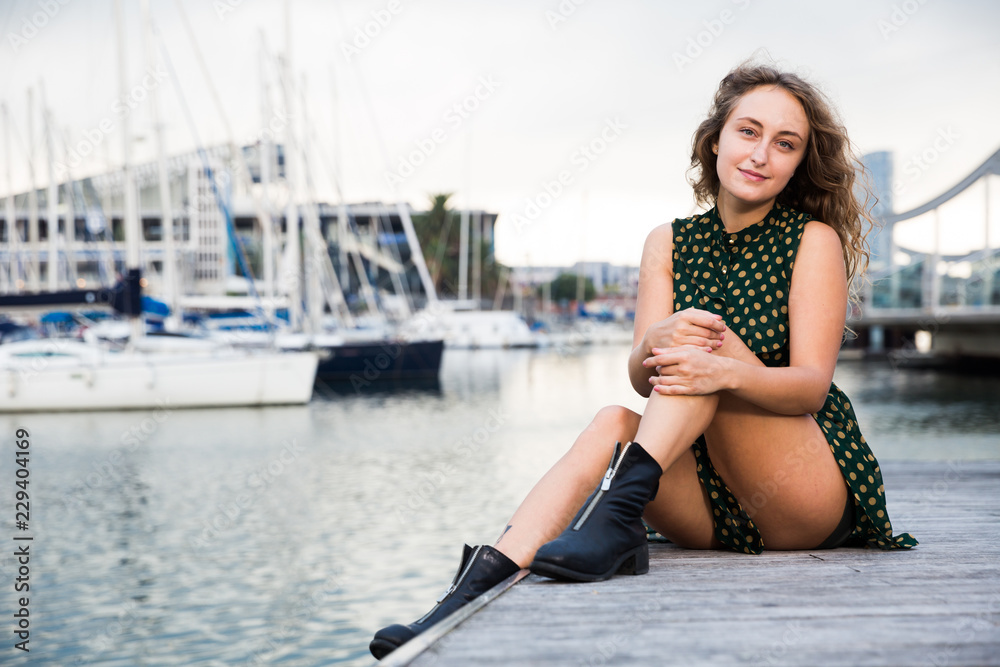 Sexy girl  in dress sitting at quay with boats  on background in  Barcelona