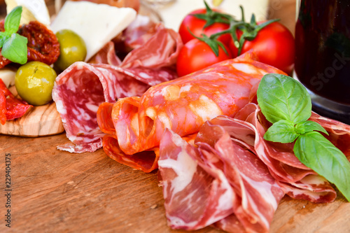 Traditional italian antipasto with prosciutto, parmesan cheese and brie cheese, sun-dried tomatoes, salami, green olives and Basil, wooden table, Italian restaurant, selective focus