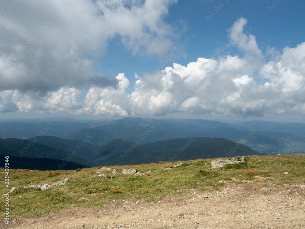 Carpathians mountains photographed from the hill, west Ukraine. Mountain pasture at summer. Big white cumulus flowing in blue sky. Ukrainian nature landscape in august. Blurred background