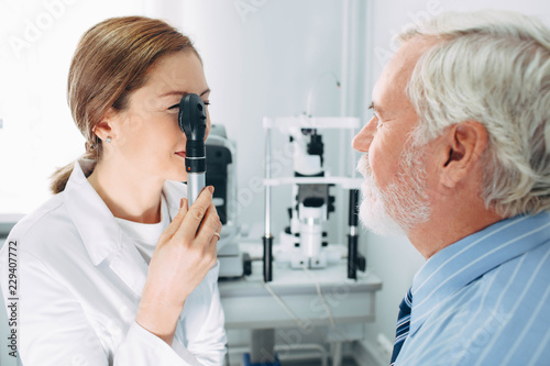 Doctor Optometrist examining old man's eyes with ophthalmoscope. Eye exam of the elderly people