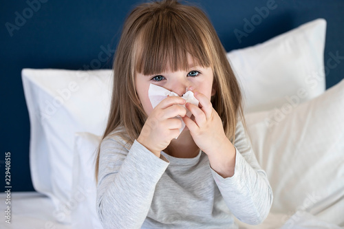 cold sick child laying on bed and blowing her nose in tissue